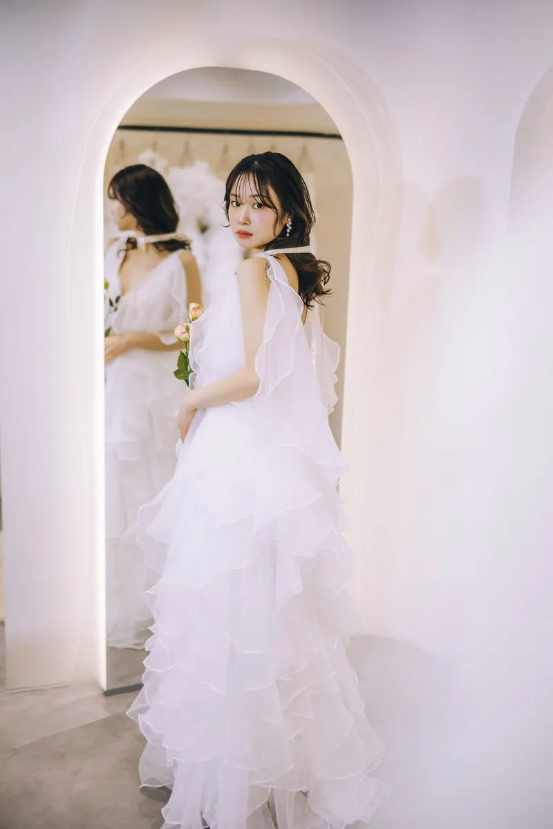 アーチ型の鏡の前に立つ、フリルのウェディングドレスを着たモデル。Dress Curreの作品
